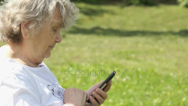 Madura anciana mujer sostiene un teléfono móvil al aire libre — Vídeo de stock