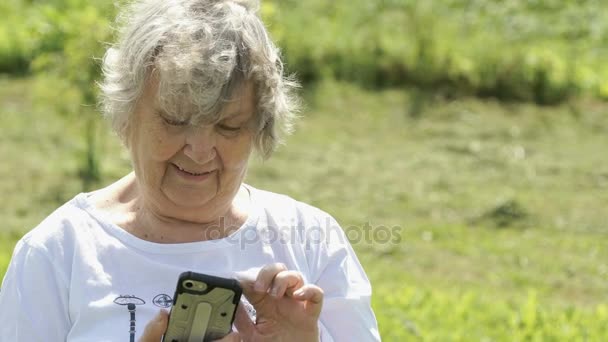 Rijpe oudere vrouw houdt een mobiele telefoon buitenshuis — Stockvideo