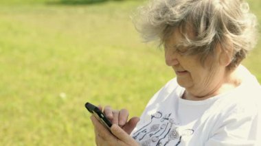 Olgun yaşlı kadın bir cep telefonu açık havada tutar