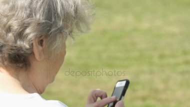 Olgun yaşlı kadın bir cep telefonu açık havada tutar