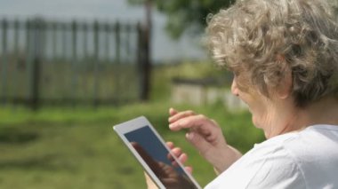 Yaşlı kadın bir gümüş bilgisayar tablet açık havada tutar