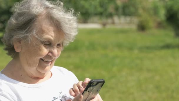 Mature elderly woman holds a mobile phone outdoors — Stock Video