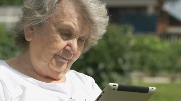 Bejaarde vrouw houdt een computer tablet buitenshuis — Stockvideo