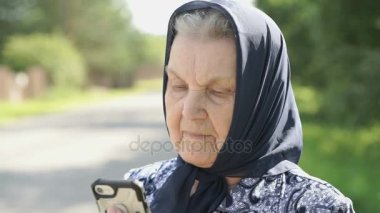 Olgun yaşlı kadın gülümseyerek smartphone açık havada gösterir