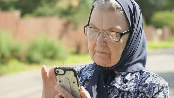Rijpe oude vrouw houdt een mobiele telefoon buitenshuis — Stockvideo