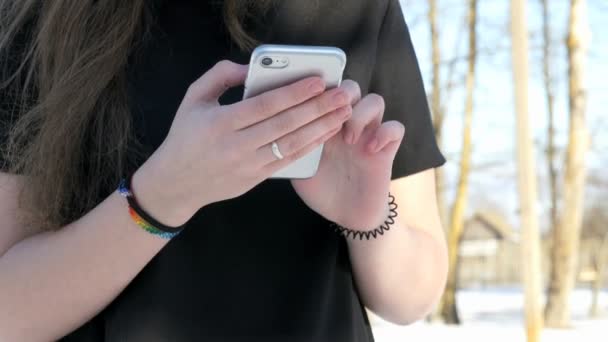 Colegiala sosteniendo un teléfono inteligente de plata al aire libre — Vídeos de Stock