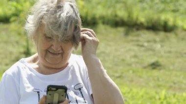 Olgun yaşlı kadın bir smartphone açık havada tutar