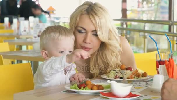 Pequeño niño sentado en la mesa se complace con la comida — Vídeos de Stock