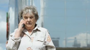 Yaşlı kadın bir akıllı telefon açık havada kullanarak konuşuyor