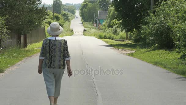 Mujer mayor caminando en la carretera en el pueblo — Vídeos de Stock