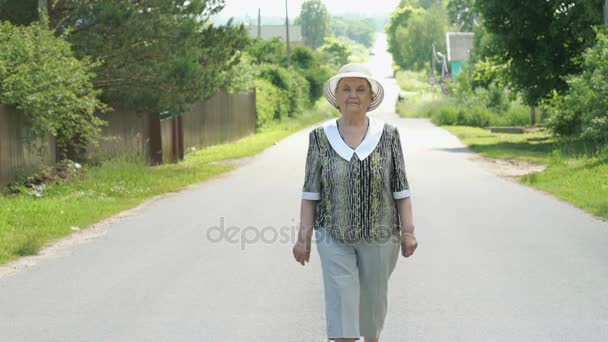 Літня жінка, що йде по дорозі в село — стокове відео