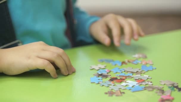 Неизвестный ребенок собирает головоломки за столом — стоковое видео