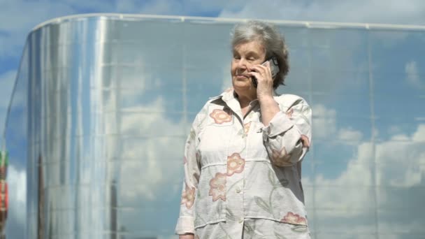 Ηλικιωμένη γυναίκα μιλά χρησιμοποιώντας ένα έξυπνο τηλέφωνο σε εξωτερικούς χώρους — Αρχείο Βίντεο