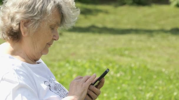 Madura anciana sostiene un teléfono inteligente al aire libre — Vídeo de stock