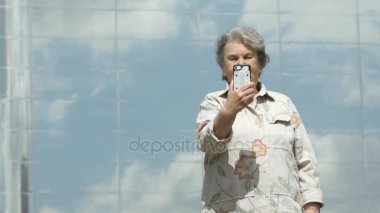 Yaşlı kadın gümüş smartphone kullanarak fotoğraf çeker