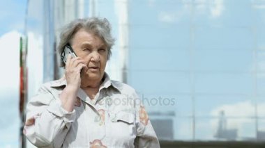 Yaşlı kadın bir akıllı telefon açık havada kullanarak konuşuyor