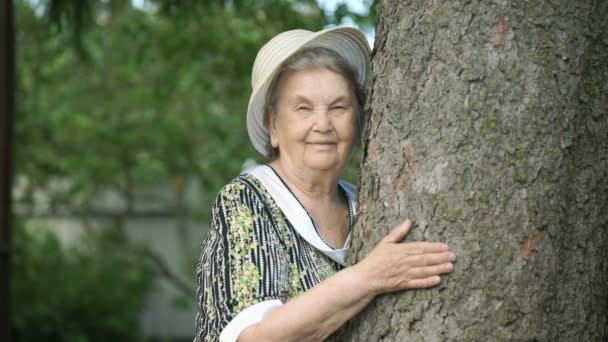 Mulher idosa abraçando árvore sorri para câmera — Vídeo de Stock