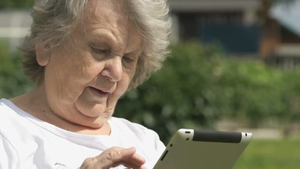 Alte Frau hält ein silbernes Computertablett im Freien — Stockvideo