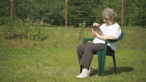 Mujer mayor sostiene una tableta de ordenador de plata al aire libre — Vídeos de Stock