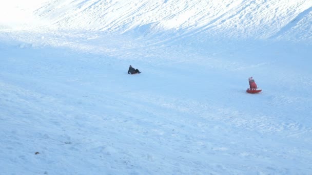 Děti sáňkování dolů z kopce na slunný zimní den — Stock video