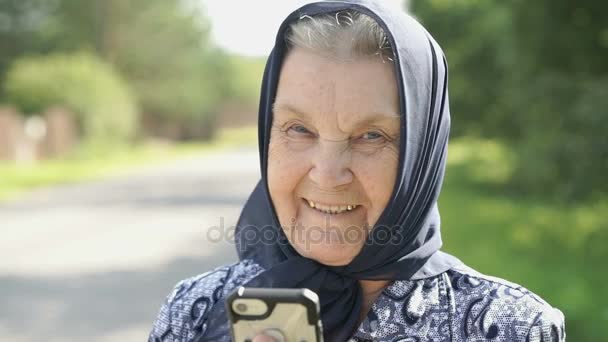 Olgun yaşlı kadın gülümseyerek smartphone açık havada gösterir — Stok video