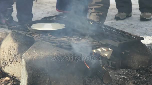 Russian pancakes on frying pan on bonfire — Stock Video