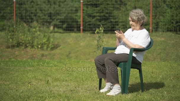 Mature old woman holds a smartphone outdoors — Stock Video