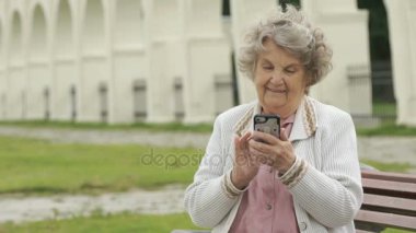 Yaşlı kadın gümüş cep telefonu açık havada tutar