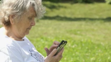 Olgun yaşlı kadın bir cep telefonu açık havada tutar