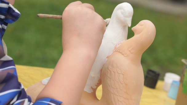 Child painting brushes on the clay figure outdoors — Stock Video