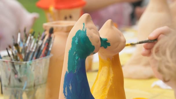 Child painting brushes on the clay figure outdoors — Stock Video