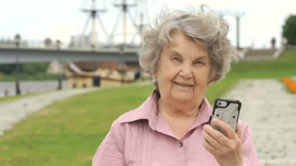 Улыбающаяся пожилая женщина показывает серебряный мобильный телефон — стоковое видео