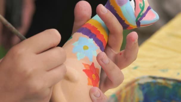 Child painting brushes on the clay figure outdoors — Stock Video