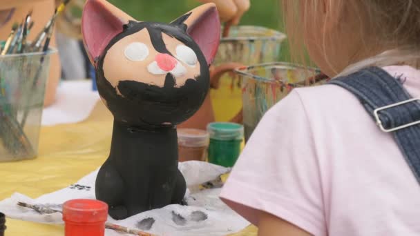 Child painting brushes on the clay figure outdoors — Stock Video