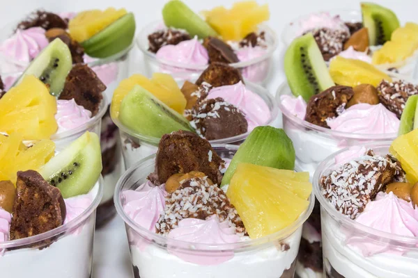 Trifle (bolo em vidro), bolos de biscoito de chocolate com creme de queijo e geléia de mirtilo, decorados com merengue, frutas (kiwi e abacaxi) e doces — Fotografia de Stock