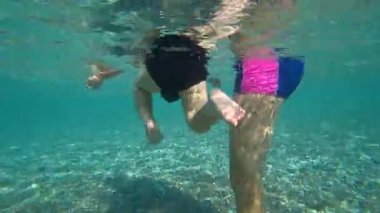 Bebek denizde suyun altında bacaklarını hareket ettiriyor. Anne kucağında çocuk.