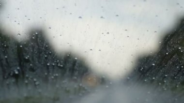 Yolda hareket eden arabanın ön camından damlayan yağmur damlaları.