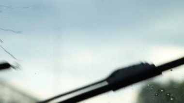 Yağmur damlaları ön cama düşer ve hareket halindeki arabanın camından aşağı iner. Silecekler temizlenir.