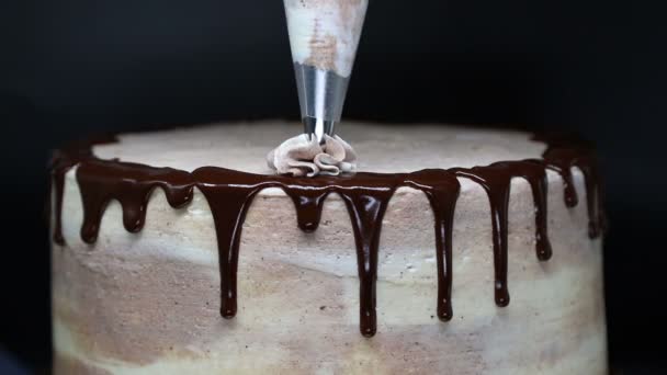 Pastel decorativo con crema. Hermoso pastel sabroso con hielo de chocolate está decorado con crema usando boquilla de pastelería . — Vídeos de Stock