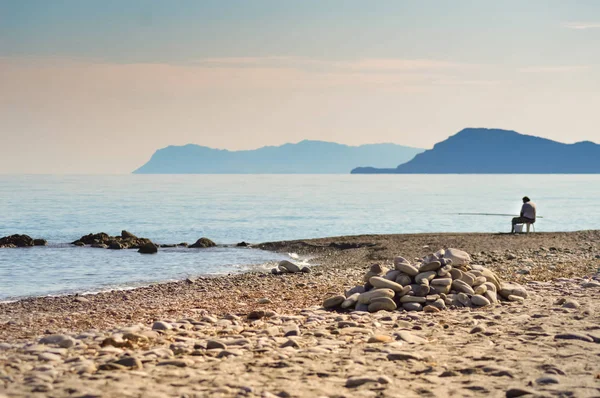 孤独的渔夫坐在圆石滩 — 图库照片