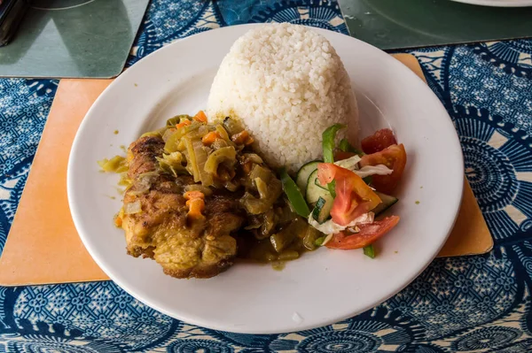 Baked chicken fillet with rice and vegetables on a white plate and a blue tablecloth.