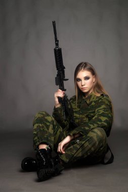 Kamuflaj kıyafeti giymiş bir kız asker stüdyoda poz veriyor.