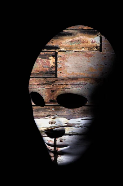 Strukturierte Maske mit rissiger Oberfläche aus rohem Holz, neutraler Ausdruck auf dunklem Hintergrund. — Stockfoto