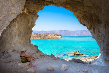 Amazing summer view of woman in a cave at Koufonisi island with magical turquoise waters, lagoons, tropical beaches of pure white sand and ancient ruins on Crete, Greece clipart