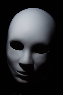 White mask with neutral expression and shadows on dark background. clipart