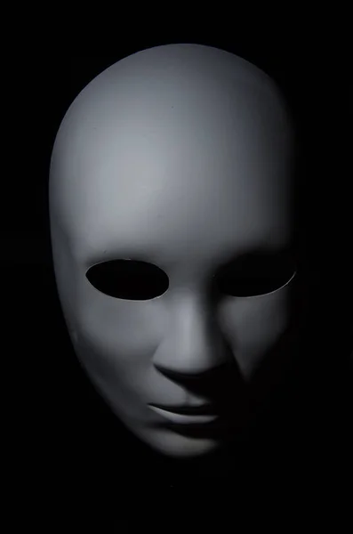 White mask with neutral expression and shadows on dark background.