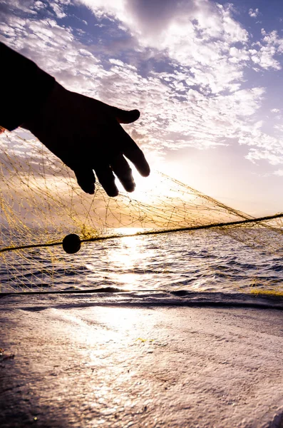 Sílhueta de mão de pescador jogando rede de pesca ao pôr do sol, Creta, Grécia — Fotografia de Stock