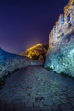 Illuminated old town of Nafplion in Greece with tiled roofs, small port, bourtzi castle, Palamidi fortress at night. clipart