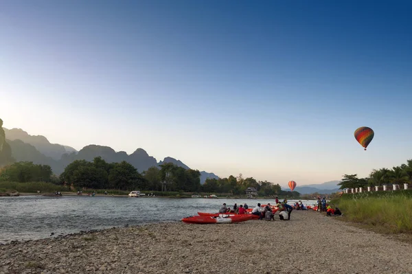 Vang Vieng, Laos - November 2015: hete lucht ballonnen vliegen over Nam lied rivier en toeristische kajaks in Vang Vieng, populaire vakantieoord in de Democratische Volksrepubliek Laos — Stockfoto