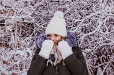 Beyaz şapkalı güzel bir genç kız ve beyaz eldivenler kusar ve karda üfler..